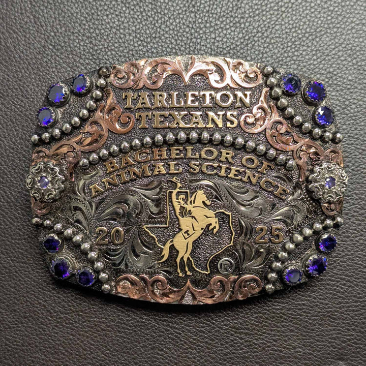 This is a Tarleton State University belt buckle featuring the Rider in Texas logo. Crafted in German silver with purple cubic zirconia, bronze words and copper scrollwork. 