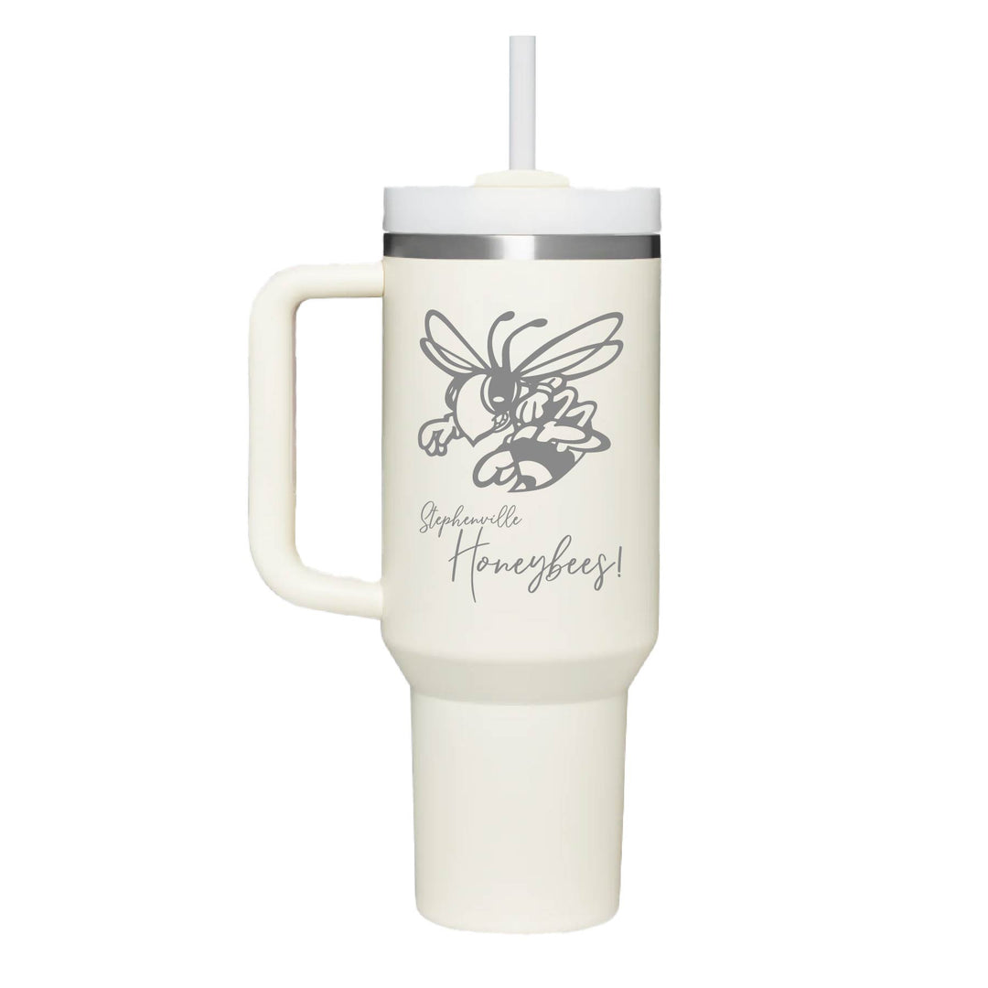 This is an insulated engraved stainless steel tumbler with a handle. The engraved image is the Stephenville Honeybees logo. The cup is cream in color. 